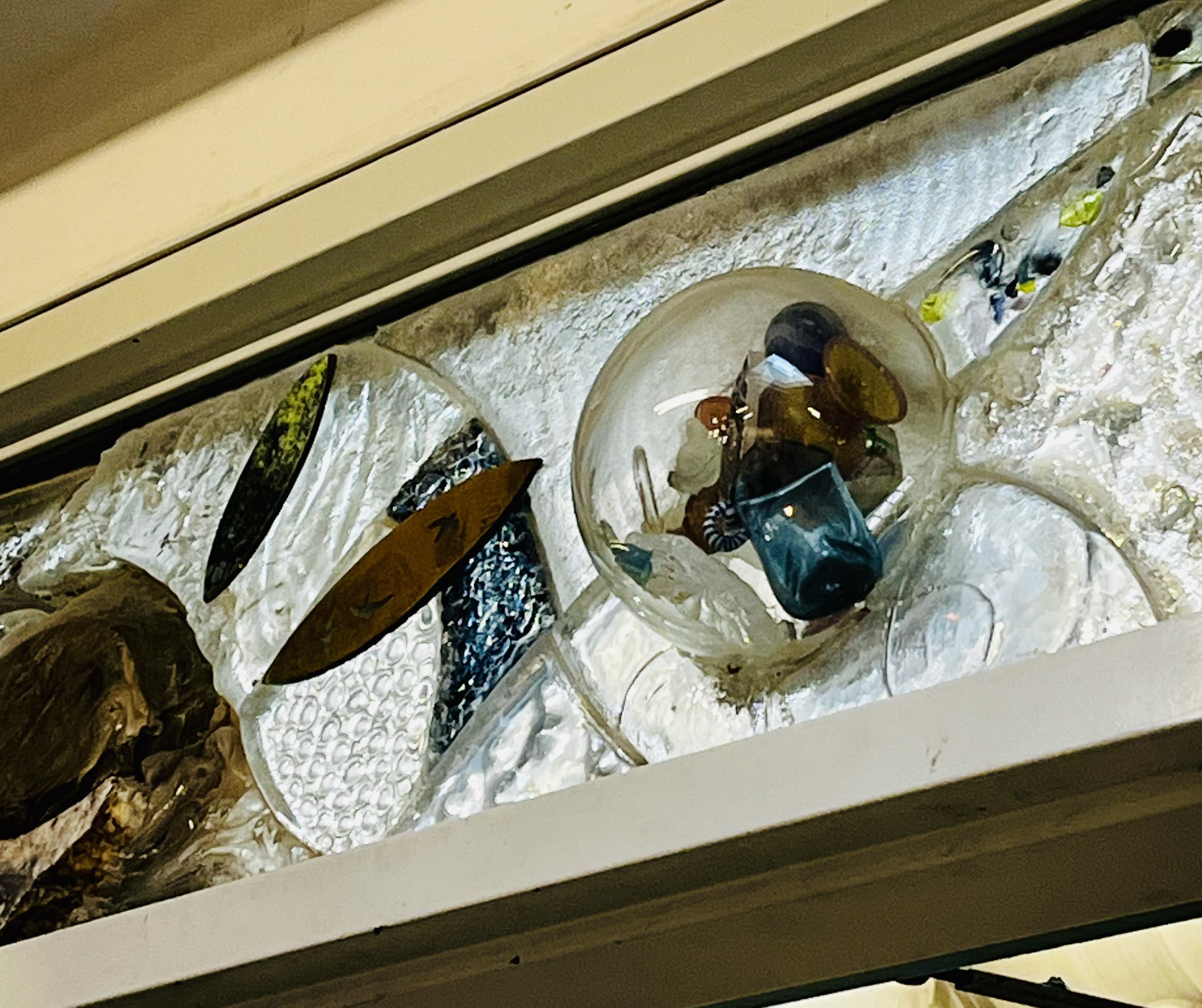 Here is the glass workshop banner in the AA wing, which is associated with the Craft and Design (glass) program.
      There's a glass orb, the inner side is visible beacause its transparency. 
      The objects inside I suppose they are also glasses but with color. 
      Glass has the ability to reflect and transmit light following geometrical optics. This presents the color in a interesting way, absorbing specific wavelengths of light while transmitting others, creating its color.