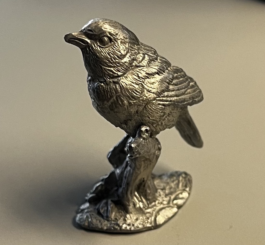 This object is made of metal. 
      <br>Color: Grey or silver 
      <br>Surface Texture: Roughly textured with intricate detailing, like feathers, wood base. Suggesting realism.
      <br>Material Plasticity: The material is hard metal so it's rigid, able to hold details in sculpting. 
      <br>Material State: Refined, the metal has been worked into a detailed sculptural form.
      <br>Material Use: Decorative figurine, sculpture, kitchen utensils.